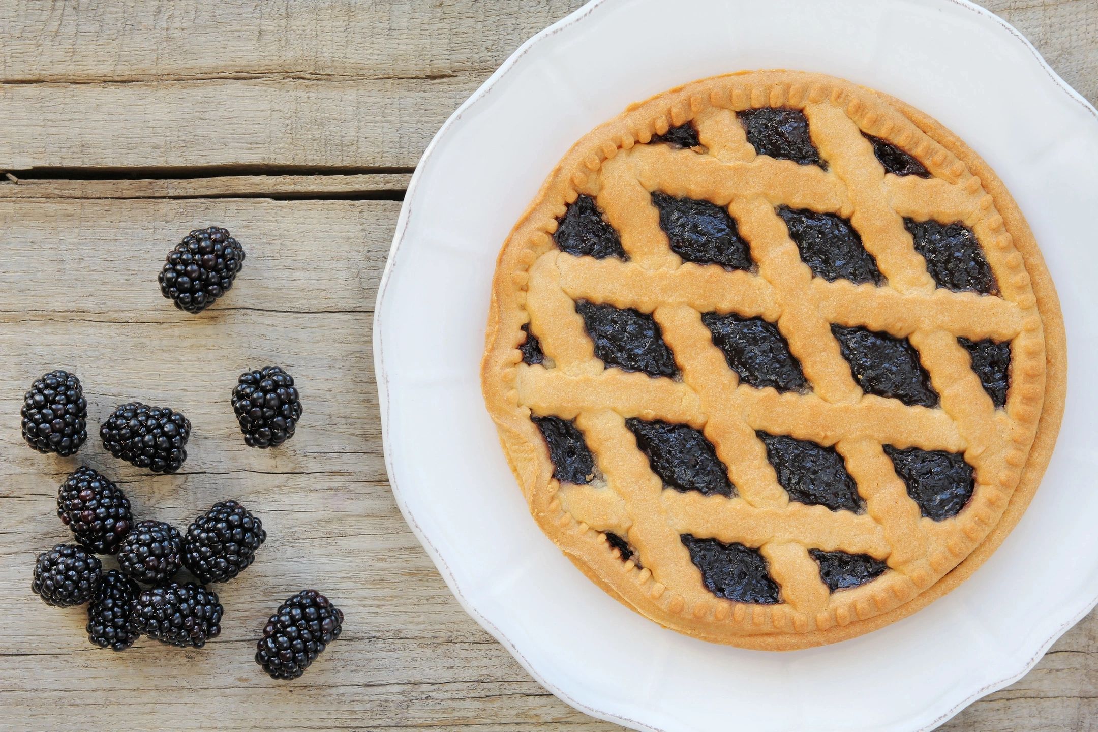 A lattice-top blackberry pie on a white plate with fresh blackberries nearby.